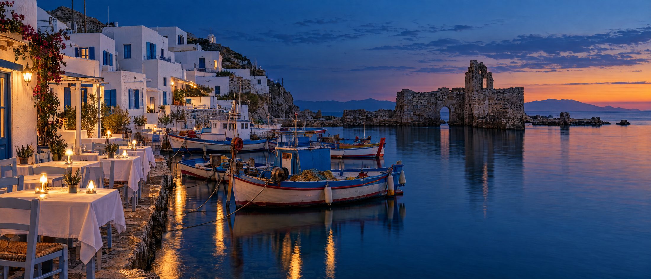 A Cycladic fishing harbour at dusk with waterside tables and a ruined Venetian fort